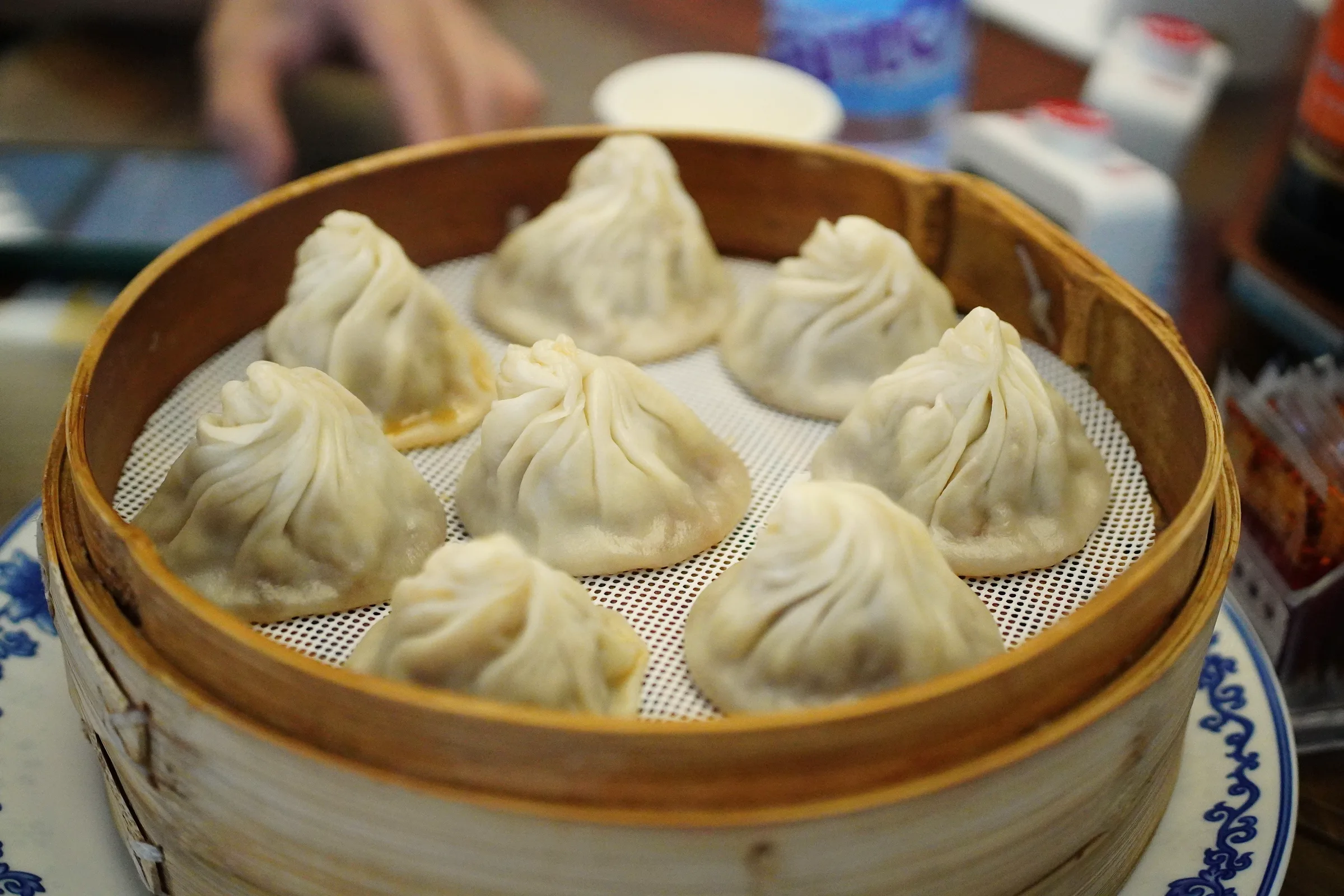 Hands closing pleats around a filled dumpling wrapper